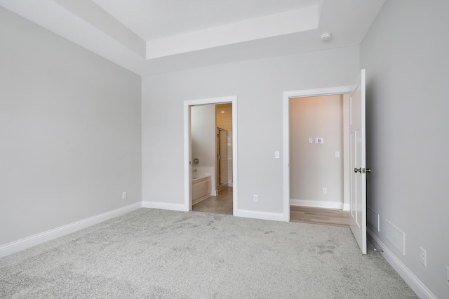 unfurnished bedroom featuring light carpet, ensuite bath, baseboards, a tray ceiling, and visible vents