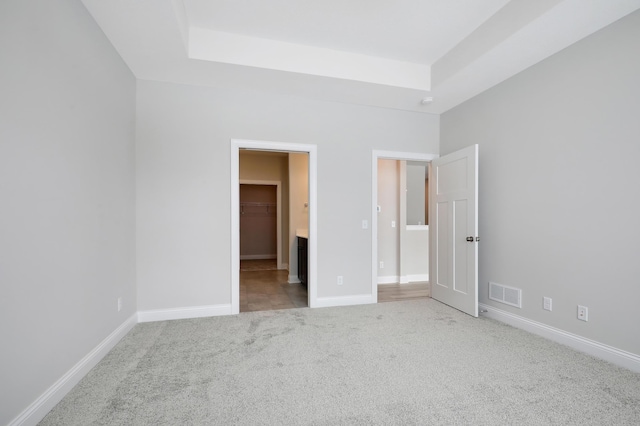 unfurnished bedroom with visible vents, a raised ceiling, carpet, and baseboards