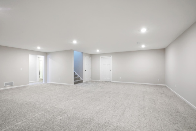 finished basement featuring visible vents, stairs, baseboards, recessed lighting, and light colored carpet