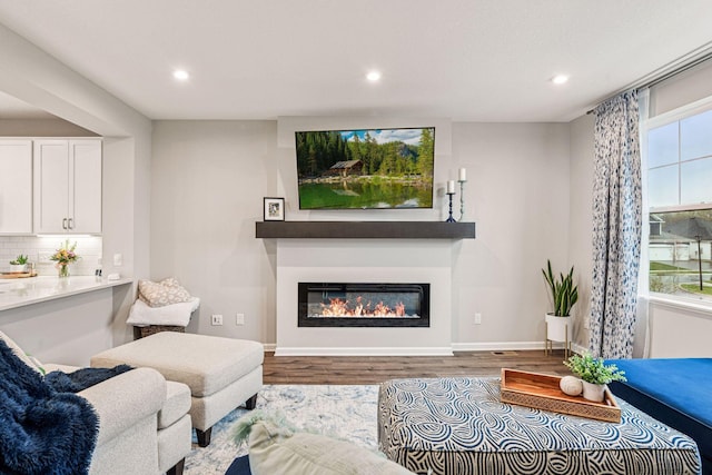 living area featuring wood finished floors, a glass covered fireplace, recessed lighting, and baseboards