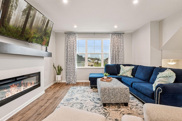 living area featuring recessed lighting, wood finished floors, a glass covered fireplace, and baseboards