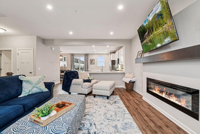 living area with dark wood finished floors, recessed lighting, a glass covered fireplace, and baseboards