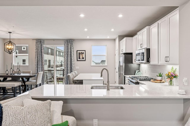 kitchen with appliances with stainless steel finishes, a sink, light stone countertops, a peninsula, and recessed lighting