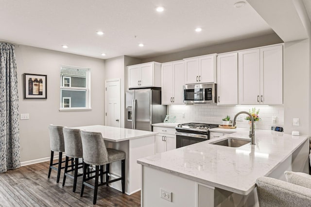 kitchen with stainless steel appliances, a sink, a kitchen breakfast bar, dark wood-style flooring, and white cabinetry