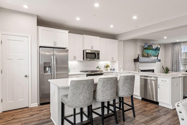 kitchen featuring appliances with stainless steel finishes, a peninsula, dark wood-type flooring, tasteful backsplash, and recessed lighting