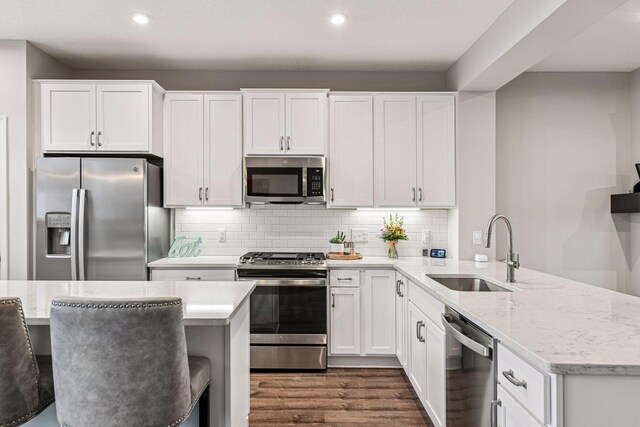 kitchen with stainless steel appliances, a sink, a peninsula, recessed lighting, and white cabinetry