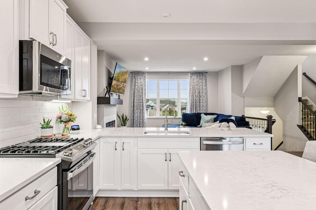 kitchen with stainless steel appliances, a sink, open floor plan, white cabinets, and decorative backsplash