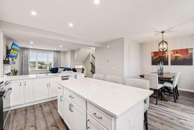 kitchen with a sink, stainless steel appliances, wood finished floors, a kitchen island, and a breakfast bar