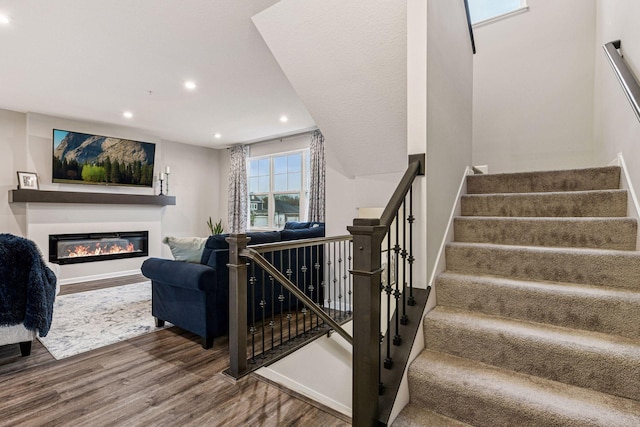 stairs with wood finished floors, recessed lighting, a glass covered fireplace, and baseboards