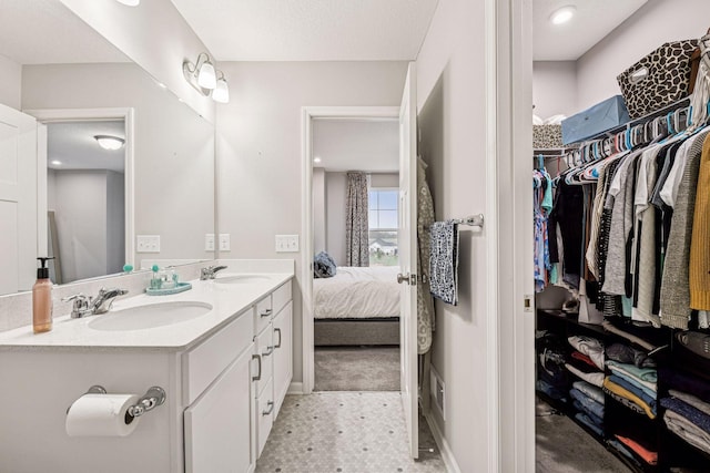 ensuite bathroom with a walk in closet, double vanity, and baseboards