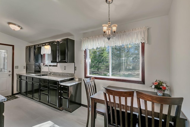 kitchen featuring a sink, tasteful backsplash, light stone counters, a chandelier, and dark cabinets