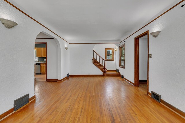 unfurnished living room with light wood-type flooring, visible vents, and arched walkways
