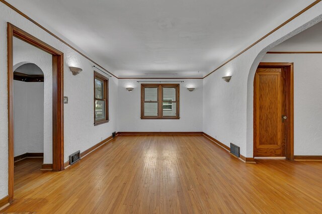 spare room with arched walkways, light wood finished floors, a textured wall, baseboards, and crown molding