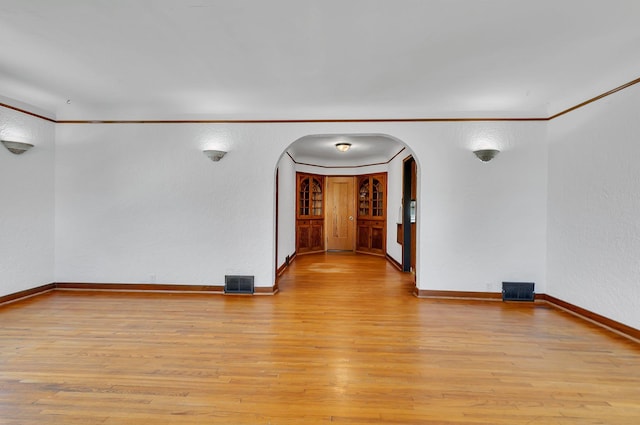 unfurnished room with arched walkways, light wood-style flooring, baseboards, ornamental molding, and a textured wall