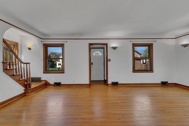 unfurnished living room featuring hardwood / wood-style floors, baseboards, crown molding, and a textured wall