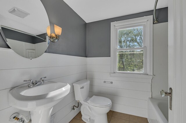 full bathroom with tile patterned floors, toilet, a tub, and a wainscoted wall