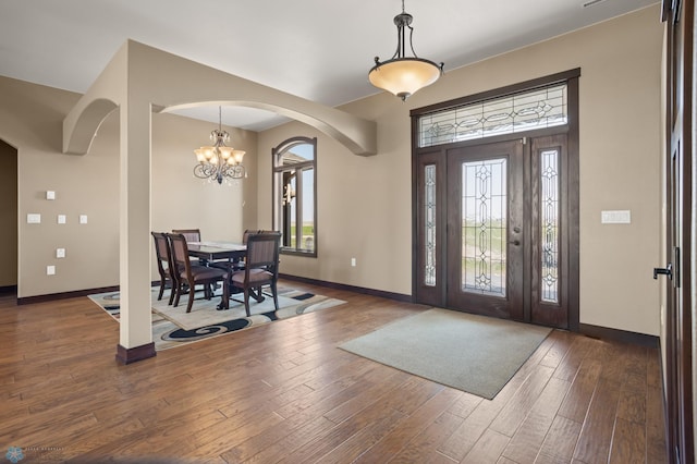 foyer entrance featuring arched walkways, a chandelier, wood-type flooring, and baseboards