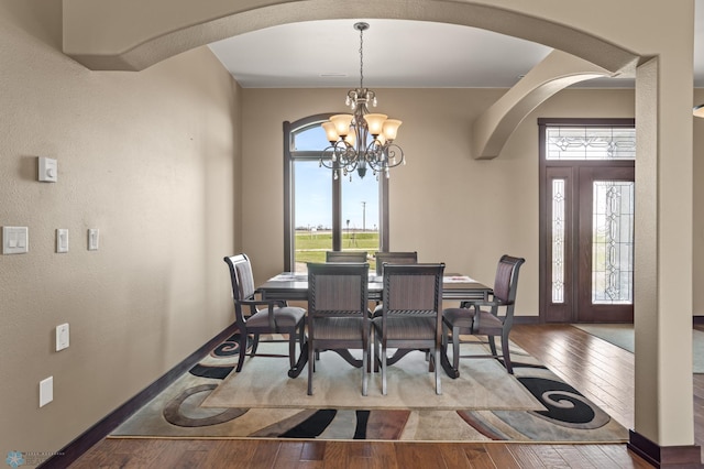 dining area featuring arched walkways, a chandelier, hardwood / wood-style floors, and baseboards