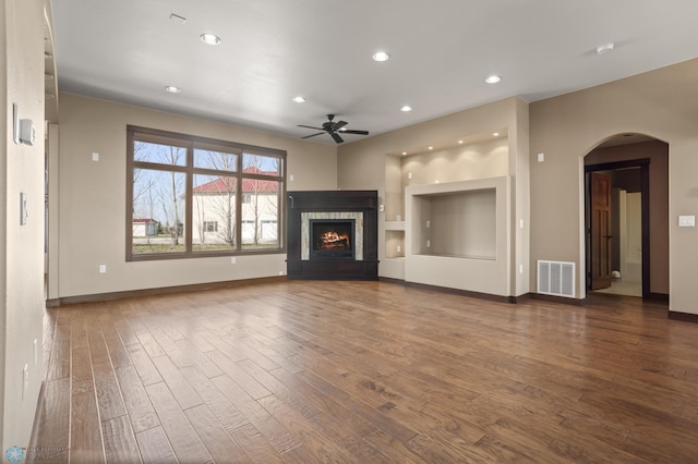 unfurnished living room with a ceiling fan, wood finished floors, arched walkways, a lit fireplace, and recessed lighting