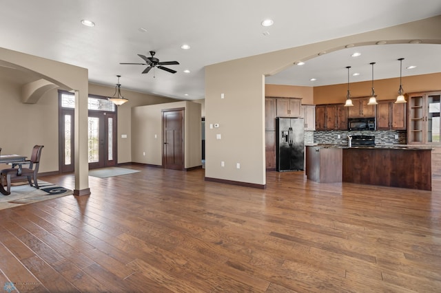 unfurnished living room with arched walkways, dark wood finished floors, ceiling fan, recessed lighting, and baseboards