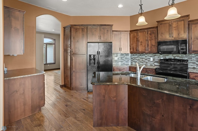 kitchen featuring black appliances, a sink, arched walkways, dark stone countertops, and hanging light fixtures