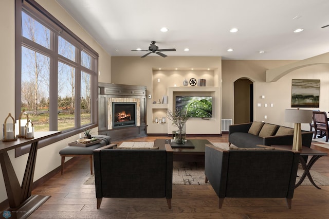 living room featuring arched walkways, a tiled fireplace, wood finished floors, ceiling fan, and recessed lighting