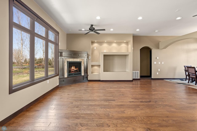 unfurnished living room with arched walkways, a ceiling fan, baseboards, recessed lighting, and a tiled fireplace