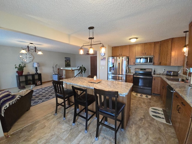 kitchen featuring a textured ceiling, decorative light fixtures, a sink, brown cabinets, and appliances with stainless steel finishes