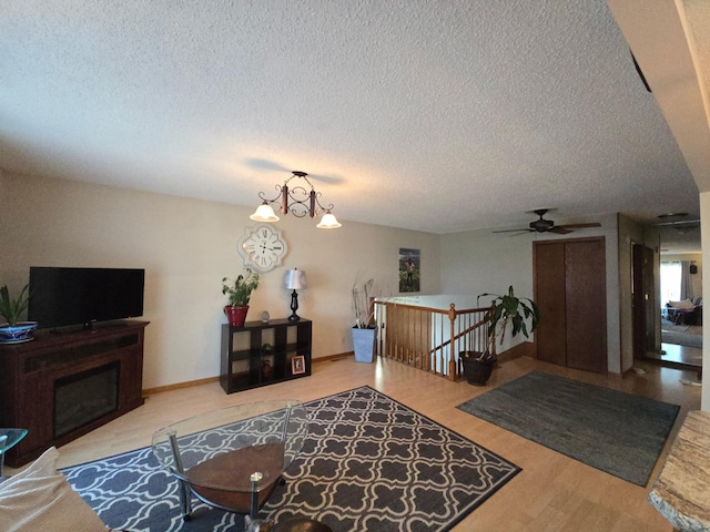 living area featuring a ceiling fan, a fireplace, a textured ceiling, and wood finished floors