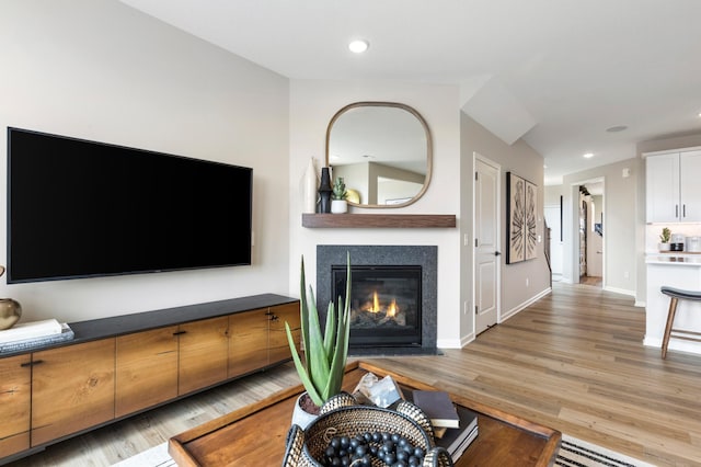 living area with light wood-style floors, a glass covered fireplace, and recessed lighting