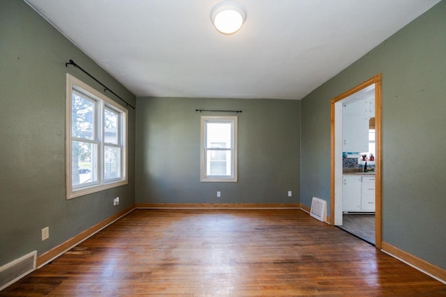 unfurnished room featuring a healthy amount of sunlight, visible vents, and wood finished floors