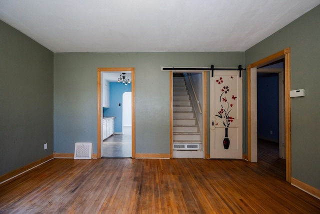 unfurnished bedroom with baseboards, a barn door, visible vents, and hardwood / wood-style flooring