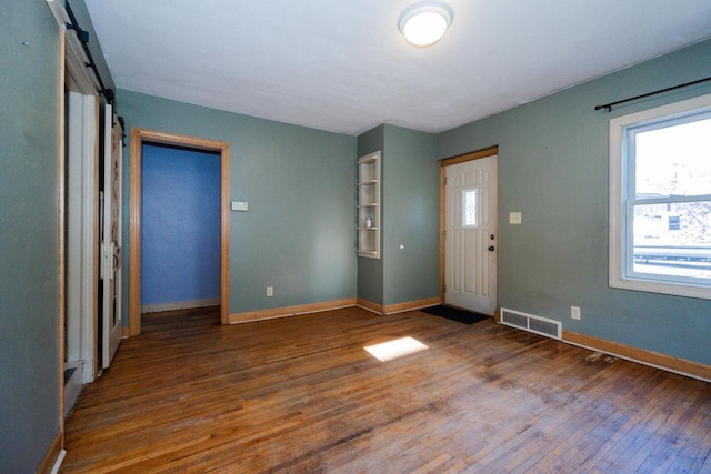 foyer entrance featuring a barn door, baseboards, visible vents, and wood finished floors