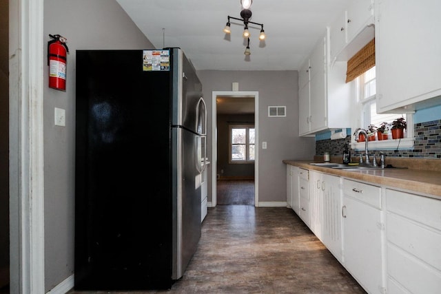 kitchen featuring a sink, freestanding refrigerator, visible vents, white cabinetry, and decorative backsplash