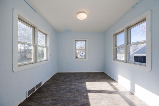 empty room with baseboards, visible vents, plenty of natural light, and wood finished floors