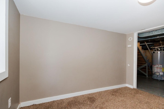 spare room featuring carpet flooring, stairway, baseboards, and gas water heater