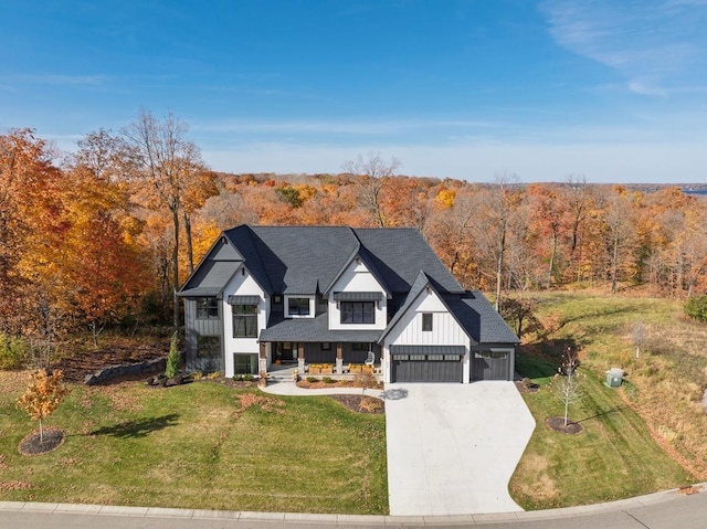 modern inspired farmhouse with board and batten siding, a wooded view, covered porch, concrete driveway, and a front lawn