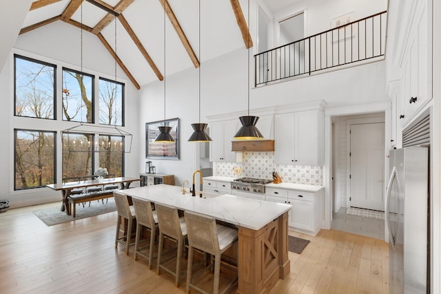 kitchen with stainless steel appliances, high vaulted ceiling, white cabinets, custom range hood, and light wood-style floors