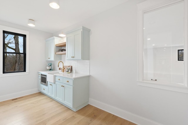 bar with light wood-style flooring, baseboards, visible vents, a sink, and tasteful backsplash