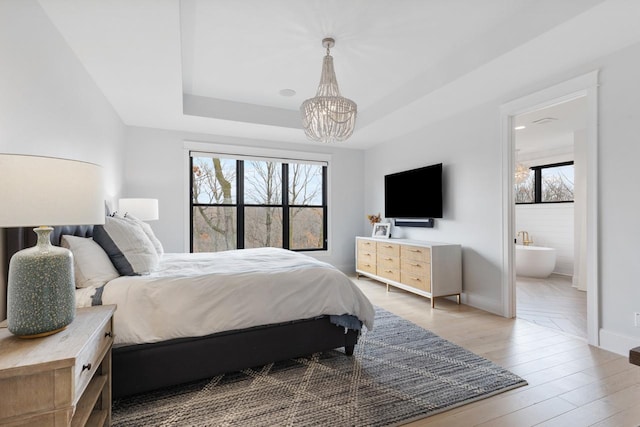 bedroom with hardwood / wood-style floors, a chandelier, a raised ceiling, connected bathroom, and baseboards
