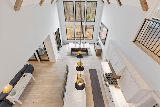 living area featuring beamed ceiling, light wood-style flooring, ceiling fan, and a high ceiling