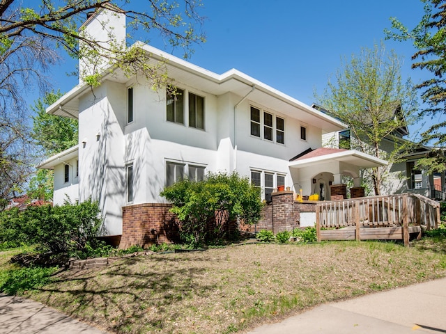 rear view of property featuring a chimney and stucco siding