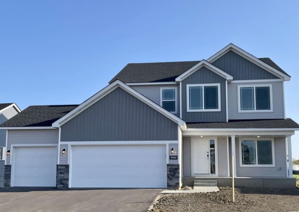 9808 32nd St NE, Saint Michael, MN 55376 - view of front of home with a porch, driveway, an attached garage, stone siding, and roof with shingles