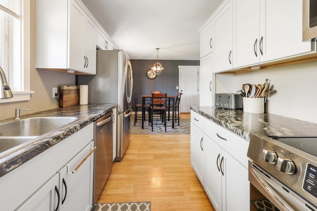 kitchen with a notable chandelier, a sink, white cabinetry, stainless steel appliances, and light wood-type flooring