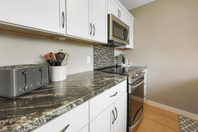 kitchen with stainless steel microwave, a toaster, light wood-style flooring, white cabinets, and electric stove