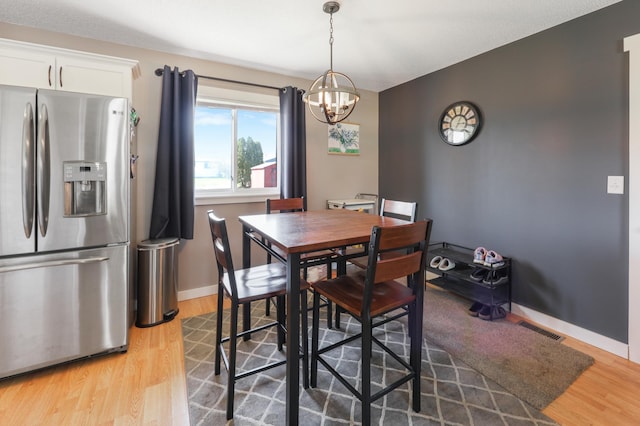 dining space with baseboards, a notable chandelier, light wood-style flooring, and visible vents