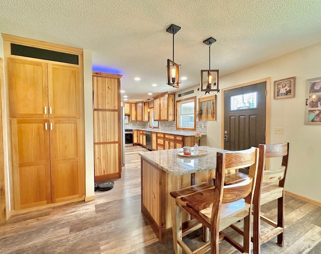 kitchen featuring light wood-type flooring, light stone counters, a kitchen bar, baseboards, and decorative light fixtures