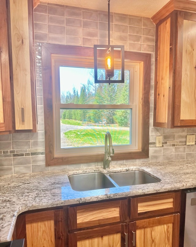 kitchen with a sink, tasteful backsplash, light stone counters, brown cabinetry, and pendant lighting