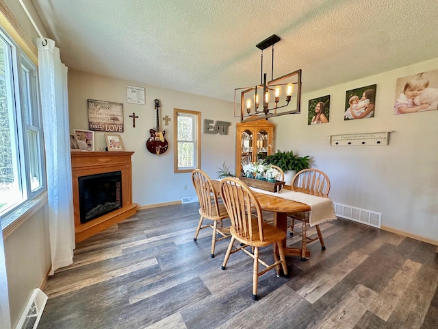 dining room featuring wood finished floors, a fireplace with raised hearth, a textured ceiling, a chandelier, and baseboards