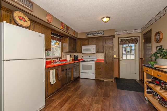 kitchen with a textured ceiling, dark wood-style floors, a sink, and white appliances